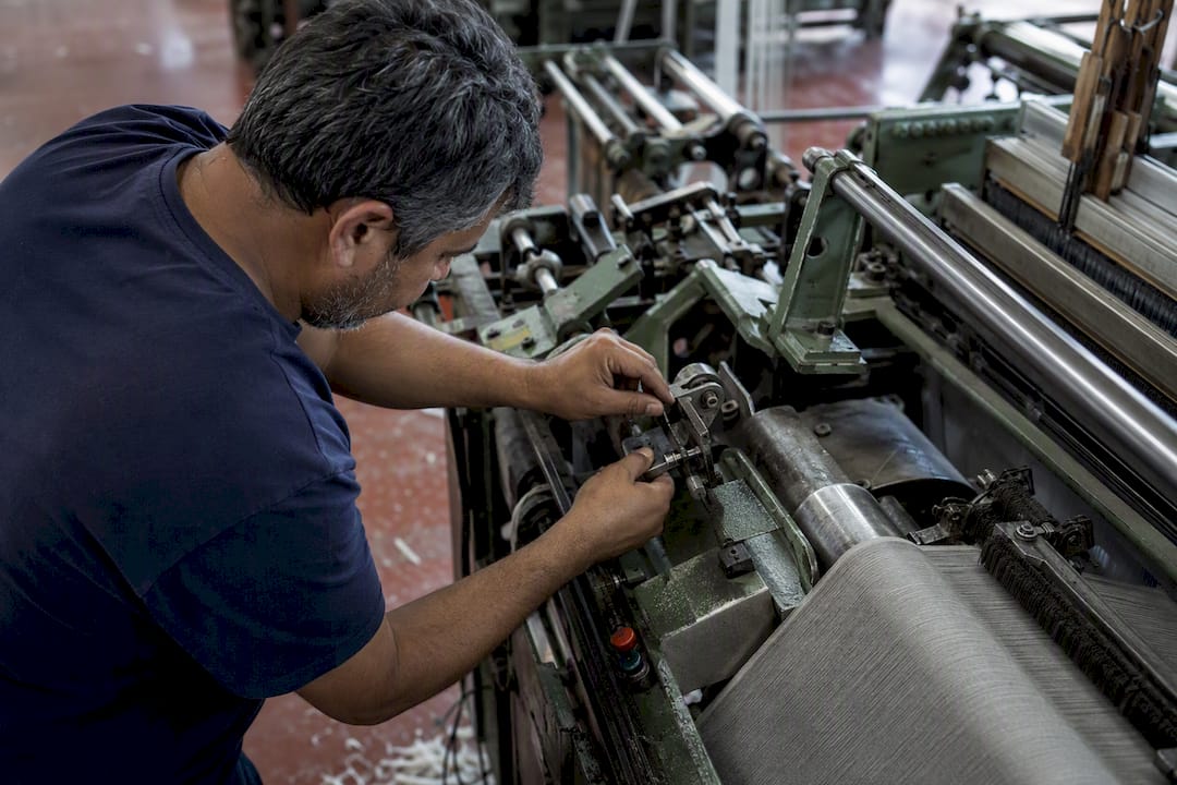 Manos ajustando componentes de una máquina textil