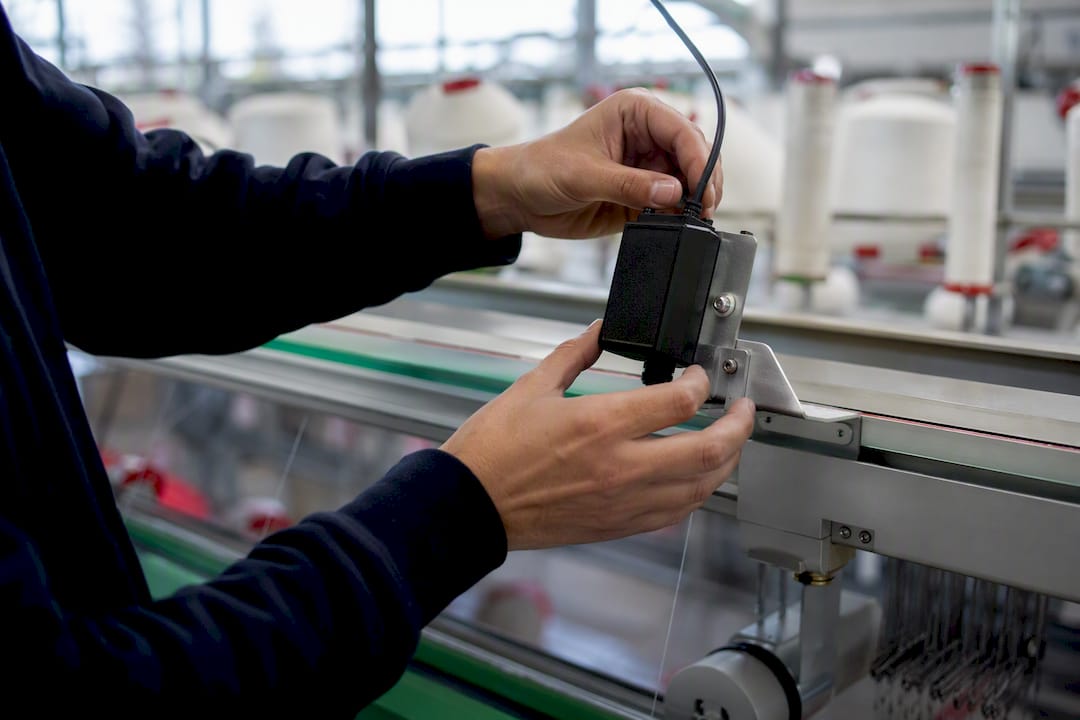 Manos ajustando un sensor en una máquina textil