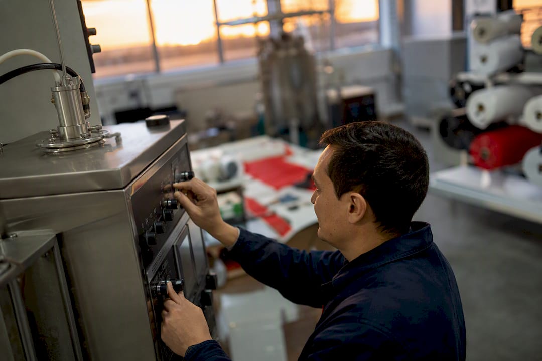 Manos ajustando los controles de una máquina piloto en una planta textil