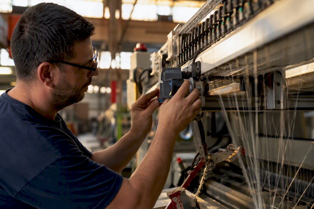 Manos de técnico ajustando el sensor de una máquina textil